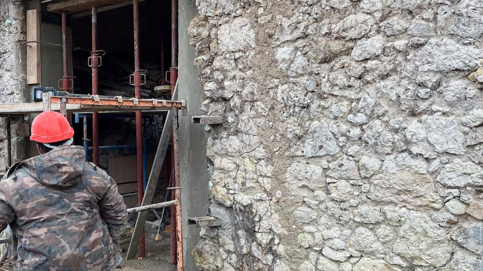 Craftsman seen from behind in front of a stone wall being restored, with scaffolding