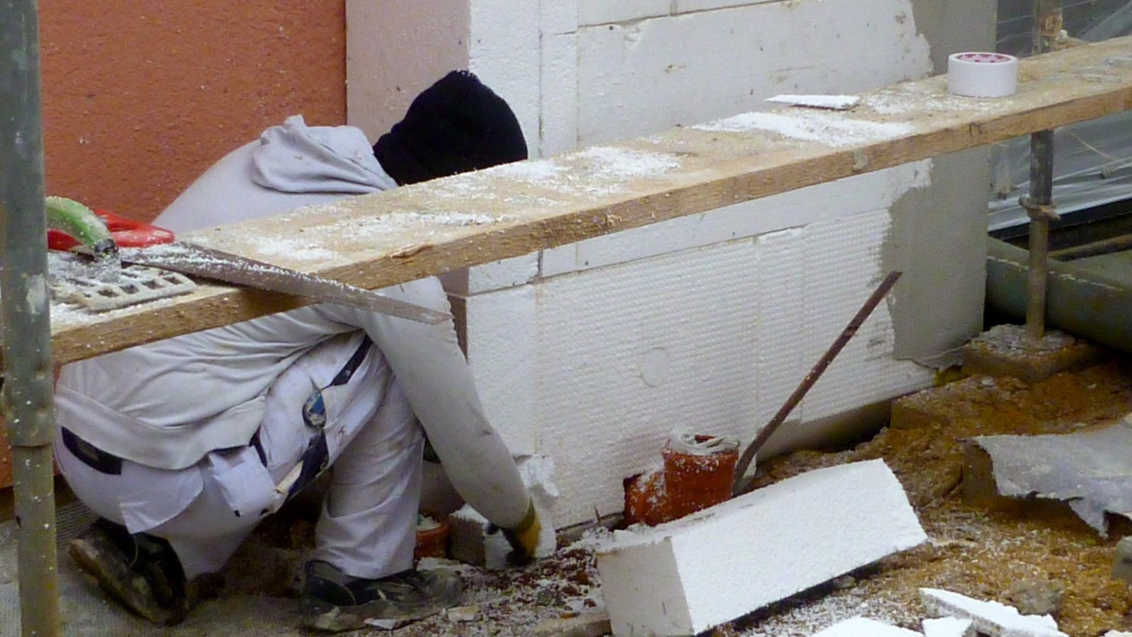 Ouvrier posant des panneaux d'isolant blanc contre un mur, pour une isolation thermique par l'extérieur