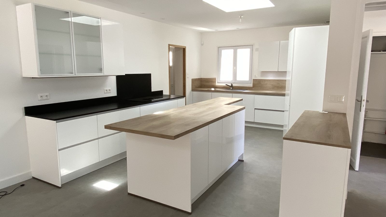 Cuisine blanche ouverte avec îlot central en bois et grandes fenêtres