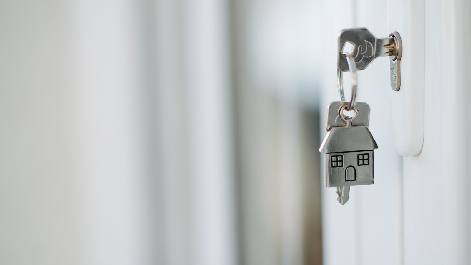 Clé de maison avec un porte-clés en forme de maison, laissée dans la serrure d'une porte blanche