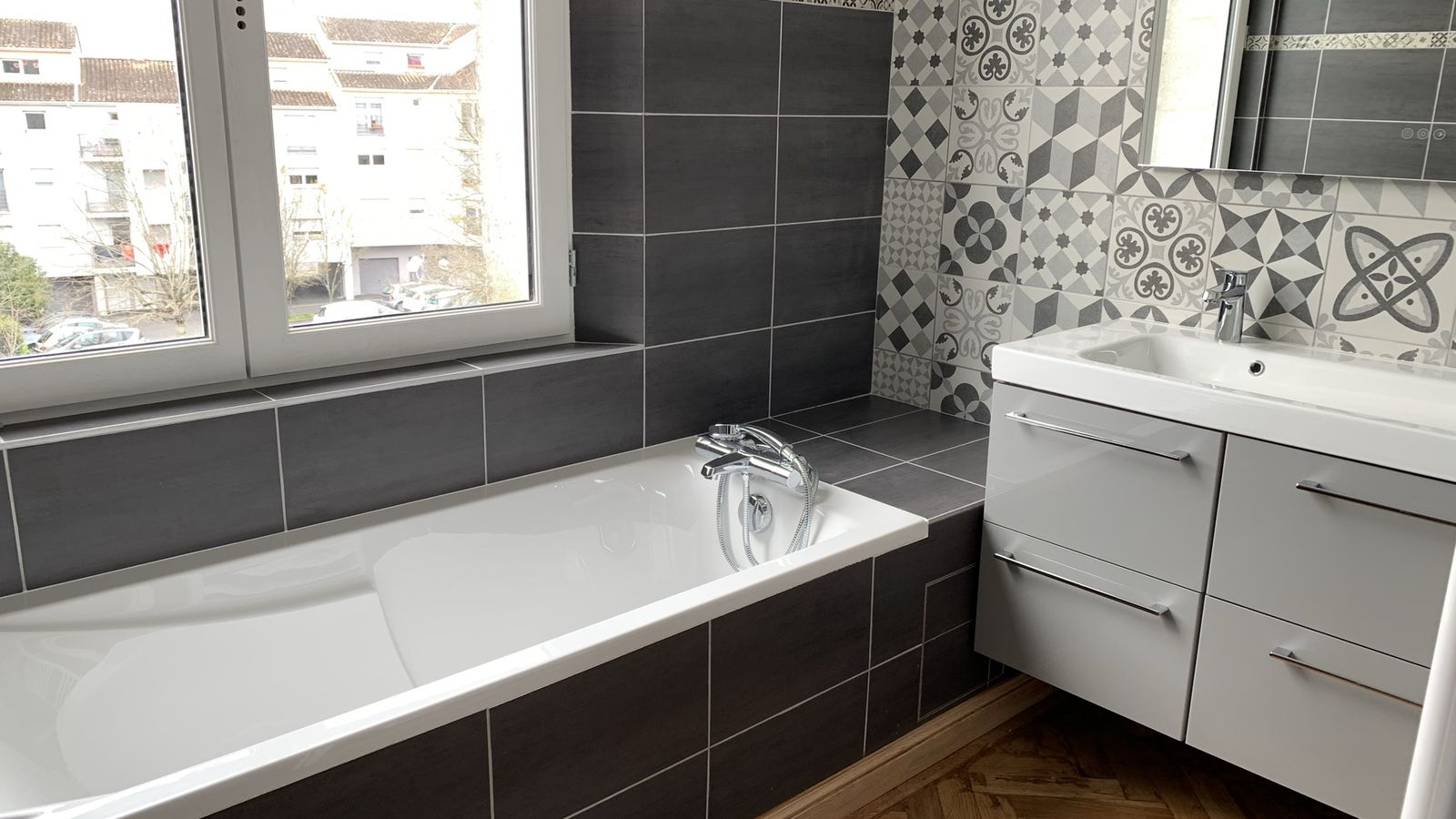 Salle de bains rénovée avec baignoire, carrelage gris anthracite et meuble vasque blanc