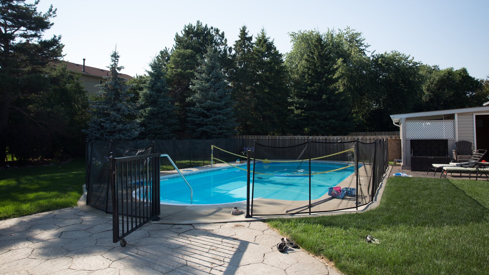 Piscine enterrée dans le jardin d'une maison, entourée d'une barrière de sécurité, avec un pool house sur la droite